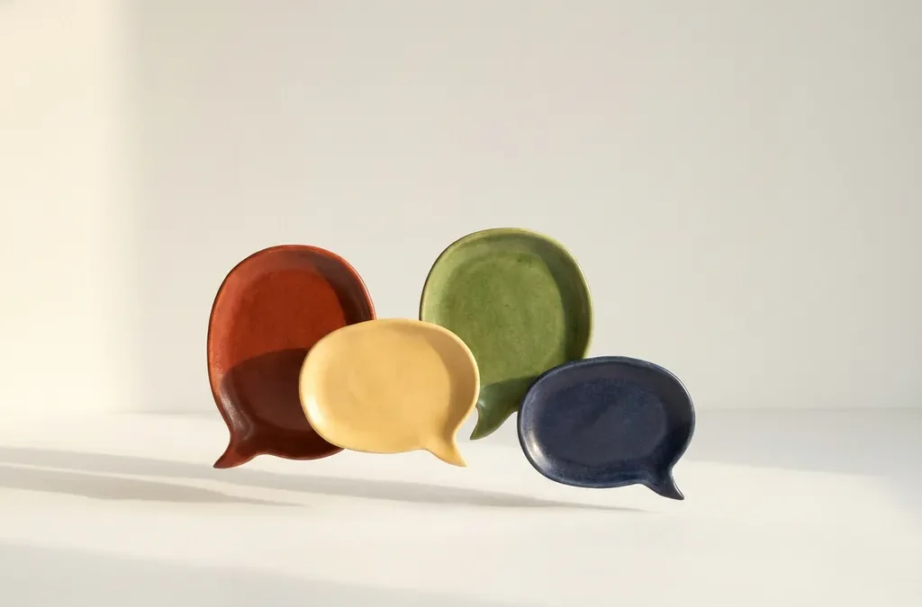 Vier keramische gespreksbellen in DISC-kleuren rood, geel, groen en blauw zweven boven wit oppervlak met zachte schaduwen