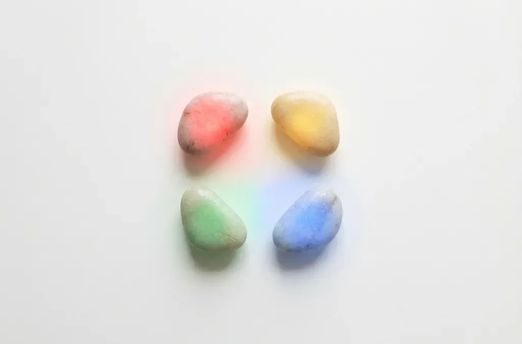 Vier gladde stenen in perfecte cirkel op witte ondergrond, verlicht in rood, geel, groen en blauw licht met gekleurde reflecties